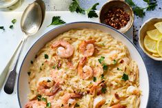 a bowl filled with pasta and shrimp next to lemon wedges