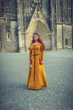 a woman in a long yellow dress standing on a cobblestone street next to a cathedral