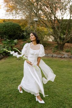 a woman in a white dress is walking through the grass