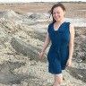 a woman in a blue dress is walking on the beach by some rocks and sand