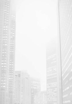 a man standing in front of tall buildings on a foggy day with his cell phone