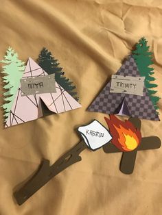 three pieces of paper cut out to look like tents and campfires on a sheet of brown fabric