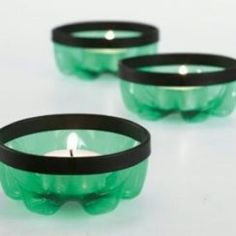 three green glass bowls with black rims on a white surface, one has a candle in it