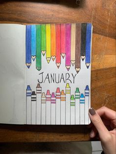 a hand holding a notebook with colored crayons on it and the words january written in black