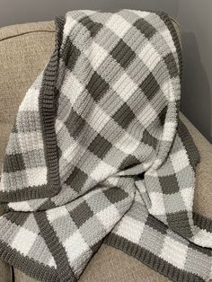 a gray and white plaid blanket sitting on top of a couch next to a pillow