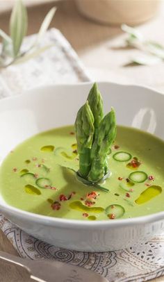 a white bowl filled with green soup and asparagus on top of the broth