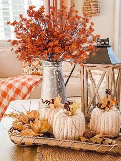 two pumpkins are sitting on a tray with fall leaves in the vase and an orange flower arrangement