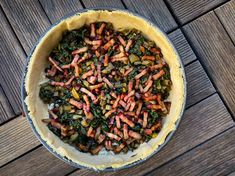 a pie with carrots and other vegetables in it on a wooden table top next to a knife