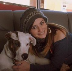 a woman sitting on top of a couch with a white and brown dog next to her