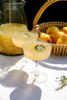 two glasses filled with drinks sitting on top of a table next to baskets of fruit