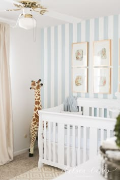 a giraffe standing next to a baby crib in a room with striped walls