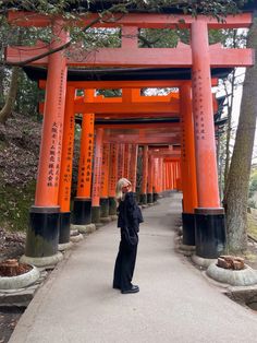 a woman standing in front of an orange torimi style structure at the end of a path