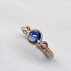 I am officially in love with this Royal Rondelle. A gorgeous blue sapphire cabochon will draw your attention right to it. Flanked by 2 diamonds which are flush set into lovely patterned accents. A modern 3 stone engagement ring with a little boho flair!I fabricated this unique setting in my studio in Tucson.<< Sapphire Specs >>Shape: round cabochonDiameter: 6mmWeight: 1.38ctQuality: FineColor: Royal BlueTreatment: Heat<< Diamond Specs >>G color, VS quality1.5mmOpen Shank: Blue Cabochon Sapphire Ring In Fine Jewelry Style, Fine Jewelry Blue Cabochon Sapphire Ring, Blue Cabochon Sapphire Ring, Wedding Sapphire Jewelry With Cabochon, Fine Jewelry Sapphire Cabochon, Sapphire Cabochon Fine Jewelry, Blue Round Cabochons For Anniversary, Blue Sapphire Cabochon Jewelry, Blue Round Gemstone Cabochons