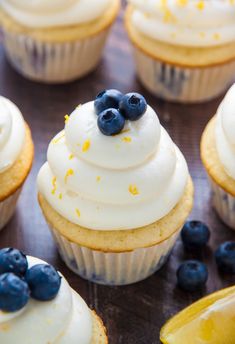 cupcakes with white frosting, blueberries and lemon wedges on a table