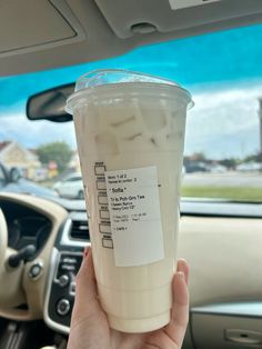 a person holding up a drink in their hand while sitting in a car with the driver's seat behind them