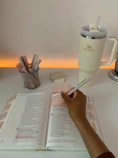 a person is writing on a book with a cup and pencils next to it