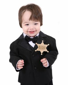 a little boy dressed in a suit and tie holding a wooden sheriff's badge