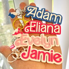 a hand holding several key chains with the words adam, elana, evelyn and jamie on them