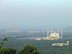 a large white building sitting on top of a lush green hillside next to a forest