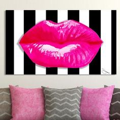 a couch with pillows and pink lips on the wall above it in front of a black and white striped background