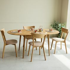 a wooden table with four chairs and plates on it in front of a white wall