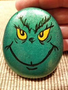 a hand holding a green painted rock with yellow eyes