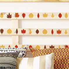 a bed topped with lots of pillows next to a wooden headboard covered in fall leaves