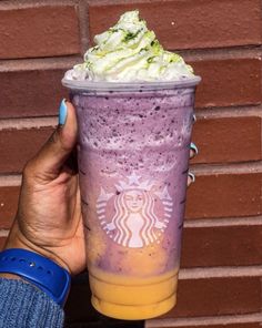 a hand holding up a purple drink with whipped cream on top