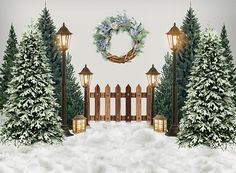 a snowy scene with christmas trees, lights and a wreath on the fence in front of it