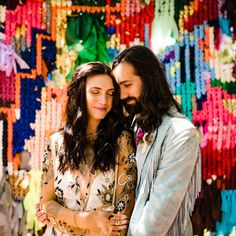 a man and woman standing next to each other in front of a wall covered with beads