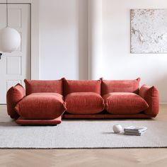 a red couch sitting on top of a wooden floor next to a white rug and lamp