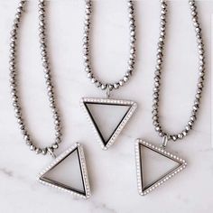 three necklaces with white stones and silver beads on a marble counter top next to each other