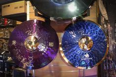 two blue and one purple cymbals hanging from the ceiling in a music store