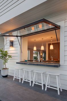 an open window on the side of a white house with three stools and a potted plant