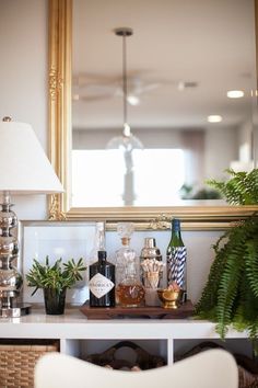 a table with plants and bottles on it in front of a mirror that has a gold frame