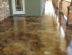 a long hallway with brown concrete floors and brick walls on both sides, leading to the front door