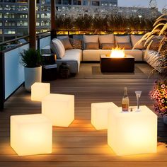 an outdoor fire pit is lit up on a deck with furniture and flowers in the foreground