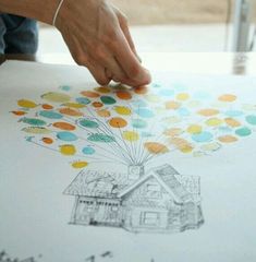 a person is drawing with colored pencils on paper while sitting at a table in front of a house