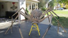 a giant spider sculpture sitting on top of a yellow step ladder in front of a house