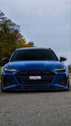 the front end of a blue sports car parked on a road with trees in the background