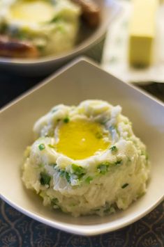 mashed potatoes with green onions and oil in a white bowl on a blue tablecloth