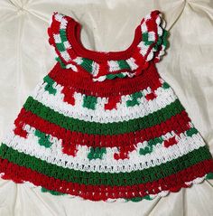 a crocheted christmas dress laying on top of a white bed sheet with red, green and white stripes