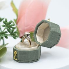 an open ring box sitting on top of a white table next to flowers and greenery