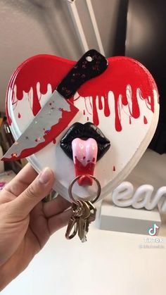 someone is holding a heart shaped keychain with blood dripping on it and a knife in the middle