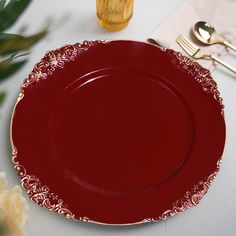 a red plate sitting on top of a white table next to silverware and flowers