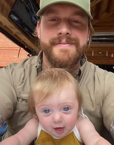 a man with a beard holding a small child in front of his face and smiling at the camera