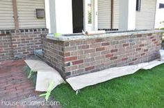 a brick wall in front of a house with grass around it and a sheet on the ground