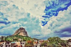 the sky is full of clouds and there are many buildings in front of this mountain