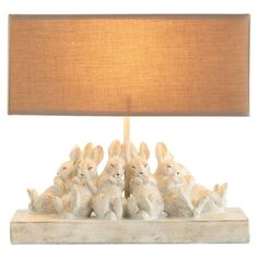 a lamp that is on top of a wooden block with rabbits sitting under it and the base has a brown shade