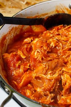 a large pot filled with meat and sauce on top of a stove next to a spatula